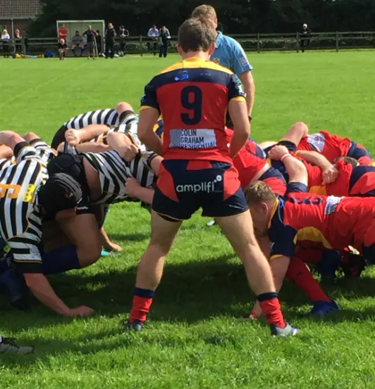 Ballyclare rugby players packing down in a scrum, with the number nine shirt carrying the Colin Graham Residential logo