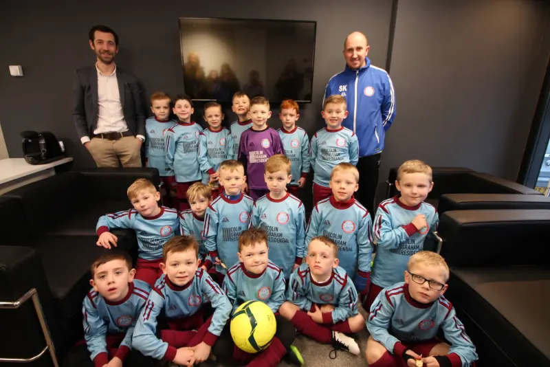 Young Carnmoney FDC players in sky blue kit with two adults from Colin Graham Residential and the club